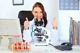 Smiling female medical doctor using microscope in laboratory and showing thumbs up
