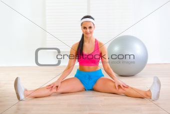 Happy flexible fitness girl stretching legs on floor at home 
