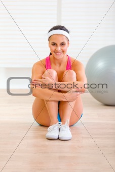 Smiling fit girl in sportswear sitting on floor at home
