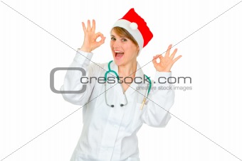 Cheerful medical doctor woman in Santa hat showing ok gesture
