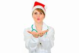 Cheerful medical doctor woman in Santa hat blowing snow 
