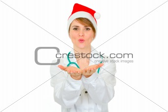 Cheerful medical doctor woman in Santa hat blowing snow 
