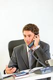 Serious modern businessman sitting at office desk and speaking phone
