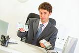 Authoritative businessman sitting at office desk and offering money packs
