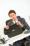 Confident businessman sitting at office desk with briefcase 
