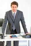 Portrait of confident modern businessman holding hands on office desk
