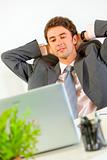 Pleased businessman relaxing on office armchair and looking in laptop
