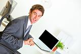 Pleased businessman  sitting at office desk and  showing yes gesture
