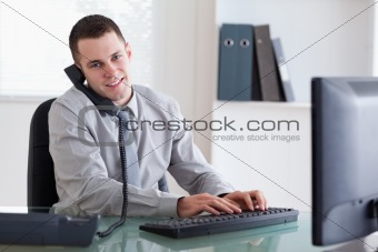 Smiling business on the phone and writing on his computer