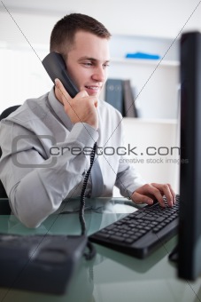 Businessman talking to costumer on the phone while using his computer
