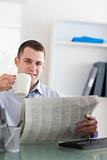 Smiling businessman reading the newspaper and having a coffee