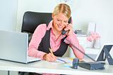 Smiling business woman talking phone and writing at notepad
