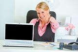 Smiling business woman showing laptops blank screen and thumbs up
