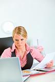 Serious modern business woman holding document and looking in laptop
