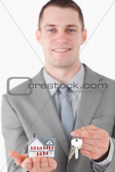 Portrait of a young businessman showing a miniature house and a set of keys
