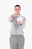 Portrait of a young businessman putting a note in a piggy bank