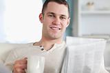 Smiling man having a tea while reading the news