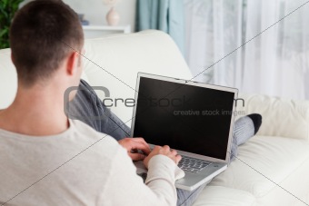 Man lying on his couch to use a laptop
