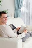 Portrait of a smiling man lying on his couch holding a book