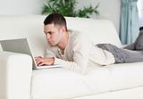 Young man lying on a sofa using a laptop