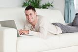 Smiling man lying on a sofa with a laptop