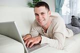 Smiling man lying on a couch with a laptop