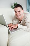 Portrait of a smiling man lying on a couch with a laptop