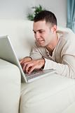 Portrait of a smiling man lying on a couch using a laptop