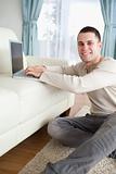Portrait of a smiling man sitting on a carpet with a laptop