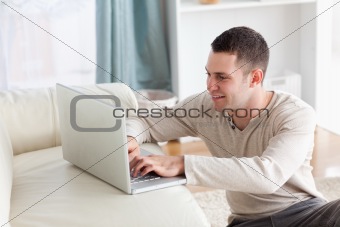 Smiling man sitting on a carpet while using a notebook