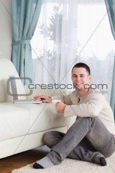 Portrait of a man sitting on a carpet with a cup of tea using a laptop