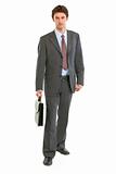 Confident modern businessman with suitcase making step
