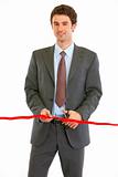 Smiling modern businessman cutting red ribbon
