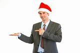 Smiling modern businessman in Santa Hat pointing on empty hand
