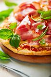 Closeup of pizza with dry cured ham and basil