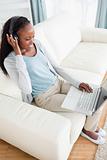 Woman on sofa listening to music and using her laptop