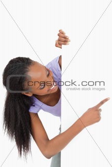 Woman looking around the corner pointing at something on white background