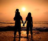 The silhouette of loving asian family walking while holding hands on beach at sunset