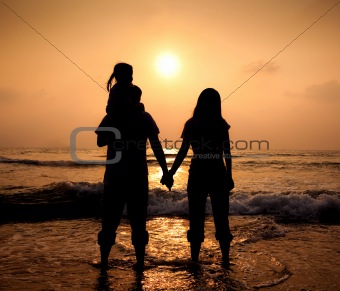 The silhouette of loving asian family walking while holding hands on beach at sunset