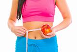 Closeup on fitness female with measuring tape around waist and apple in hand
