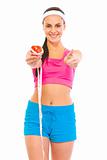 Smiling fitness female holding apple with measuring tape and showing thumbs up
