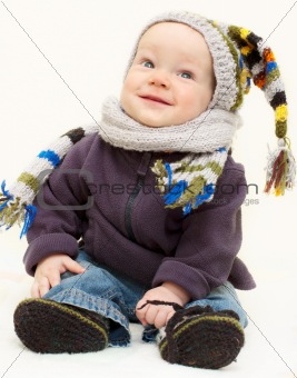 Cute baby boy in knitted handmade hat, scarf and bootees is sitt