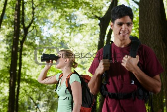 young man and woman hiking in forest with binoculars