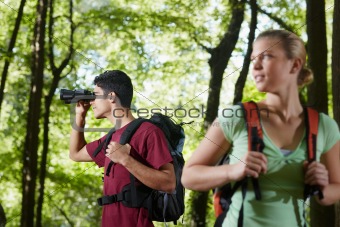 young man and woman hiking in forest with binoculars
