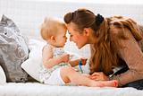 Cute baby with soother and young mom playing on divan