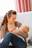 Young mother sitting on sofa and feeding her baby 
