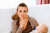 Young mama holding sleeping baby and showing shh gesture

