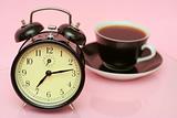 The black alarm clock and black cup from coffee is on a pink background