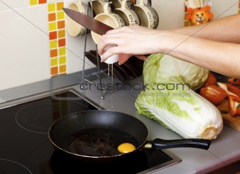 Woman cracking eggs into frying pan in kitchen 