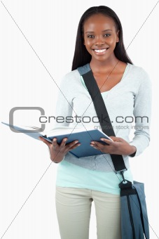 Smiling young student with bag reading in her book